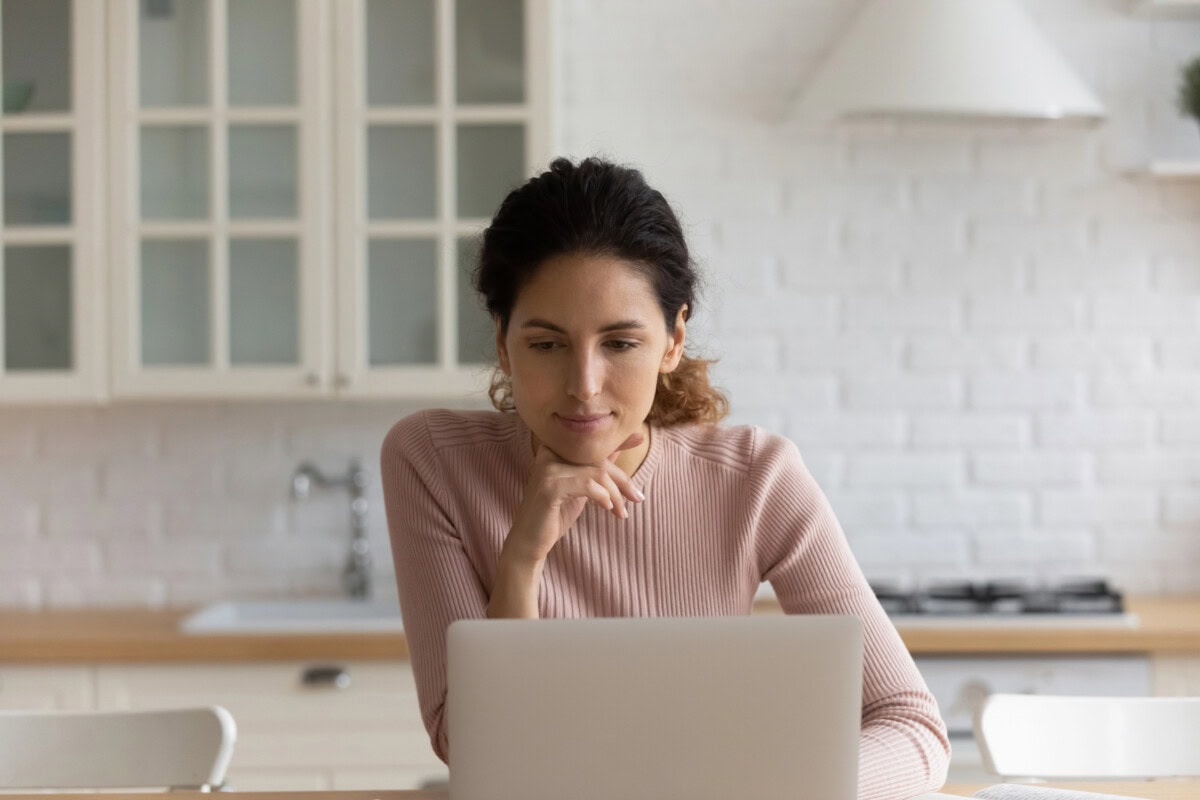 Hispanic woman sit in kitchen web surfing using laptop